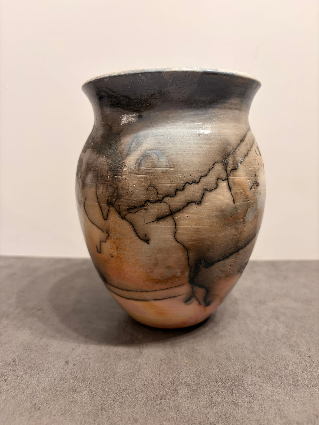 A hand-painted ceramic vase with a rounded body, featuring a marbled pattern of black, gray, beige, and brown tones, set against a neutral background.