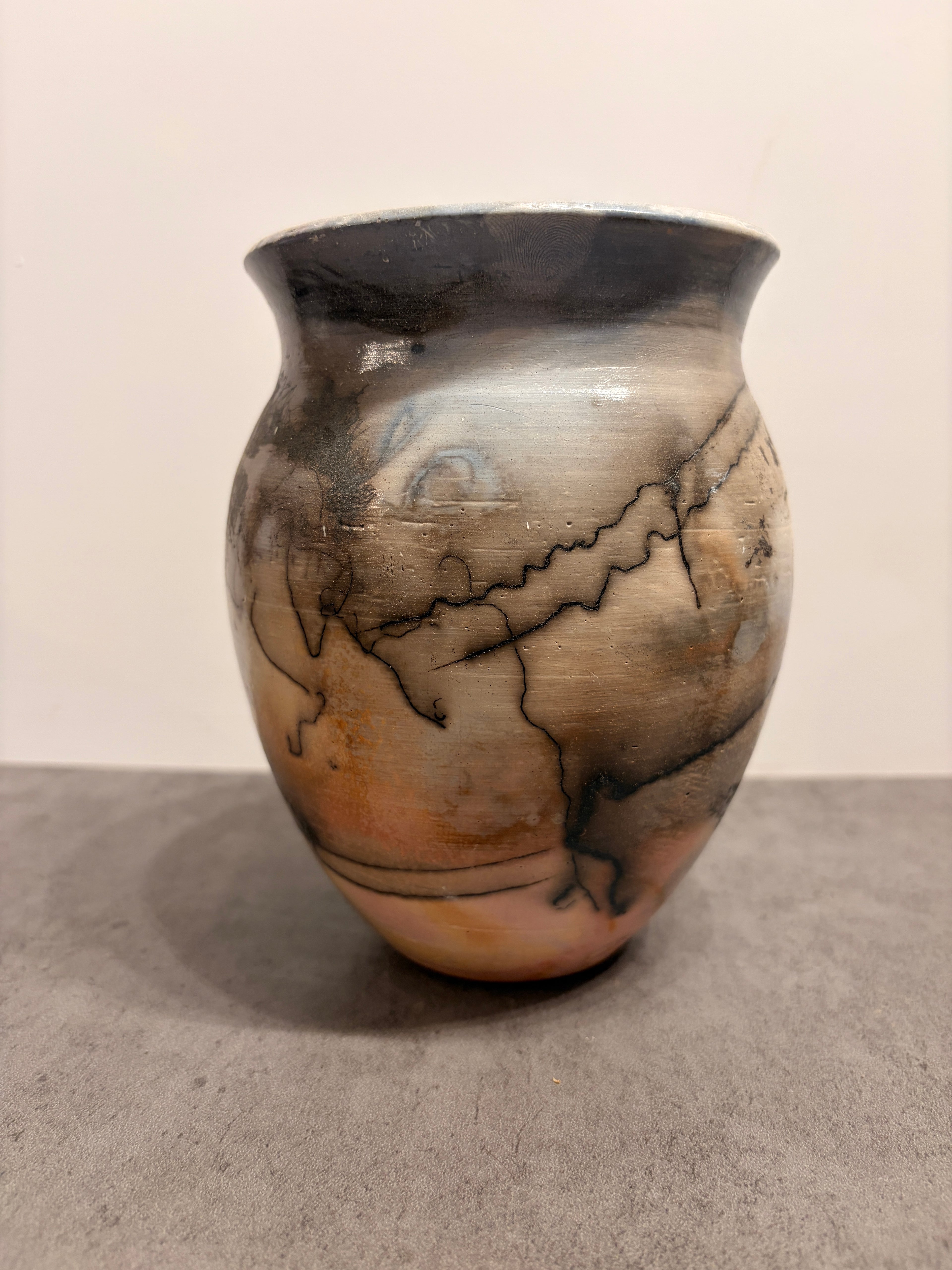 A hand-painted ceramic vase with a rounded body, featuring a marbled pattern of black, gray, beige, and brown tones, set against a neutral background.