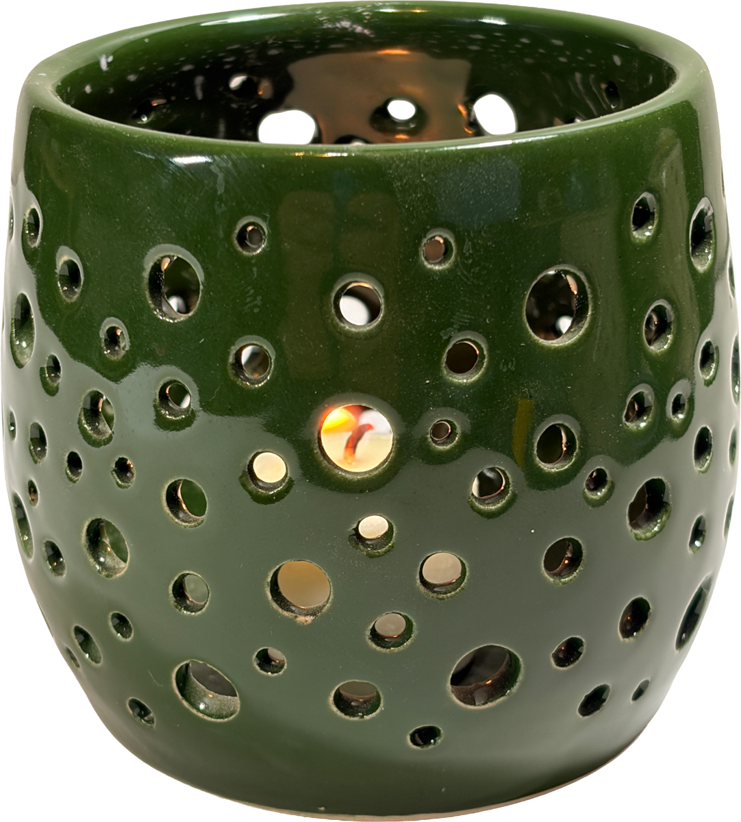 A dark green ceramic candle warmer with a glossy finish and multiple circular cutouts, shown lit with a warm glow visible through the holes.