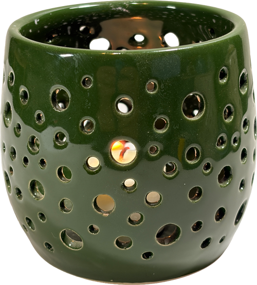 A dark green ceramic candle warmer with a glossy finish and multiple circular cutouts, shown lit with a warm glow visible through the holes.