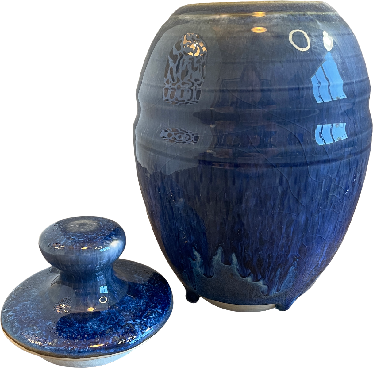A glossy cobalt blue ceramic jar with a matching lid, displayed on a clean white background. The jar features a textured, crackled glaze with lighter blue and white veining, and the lid has a matching rounded knob.