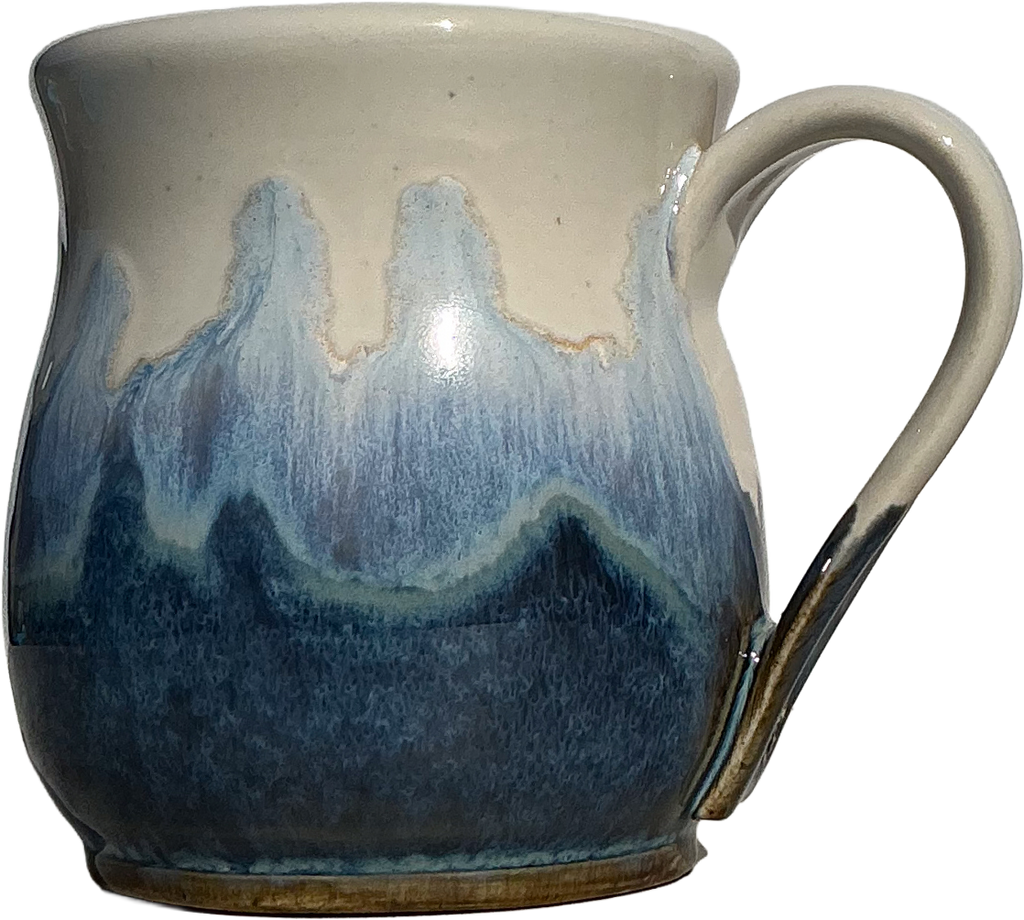 A handmade ceramic mug with a cream-colored glazed top and handle, featuring a dripping blue and navy blue glaze pattern resembling waves or mountains, with a brown clay showing at the base.