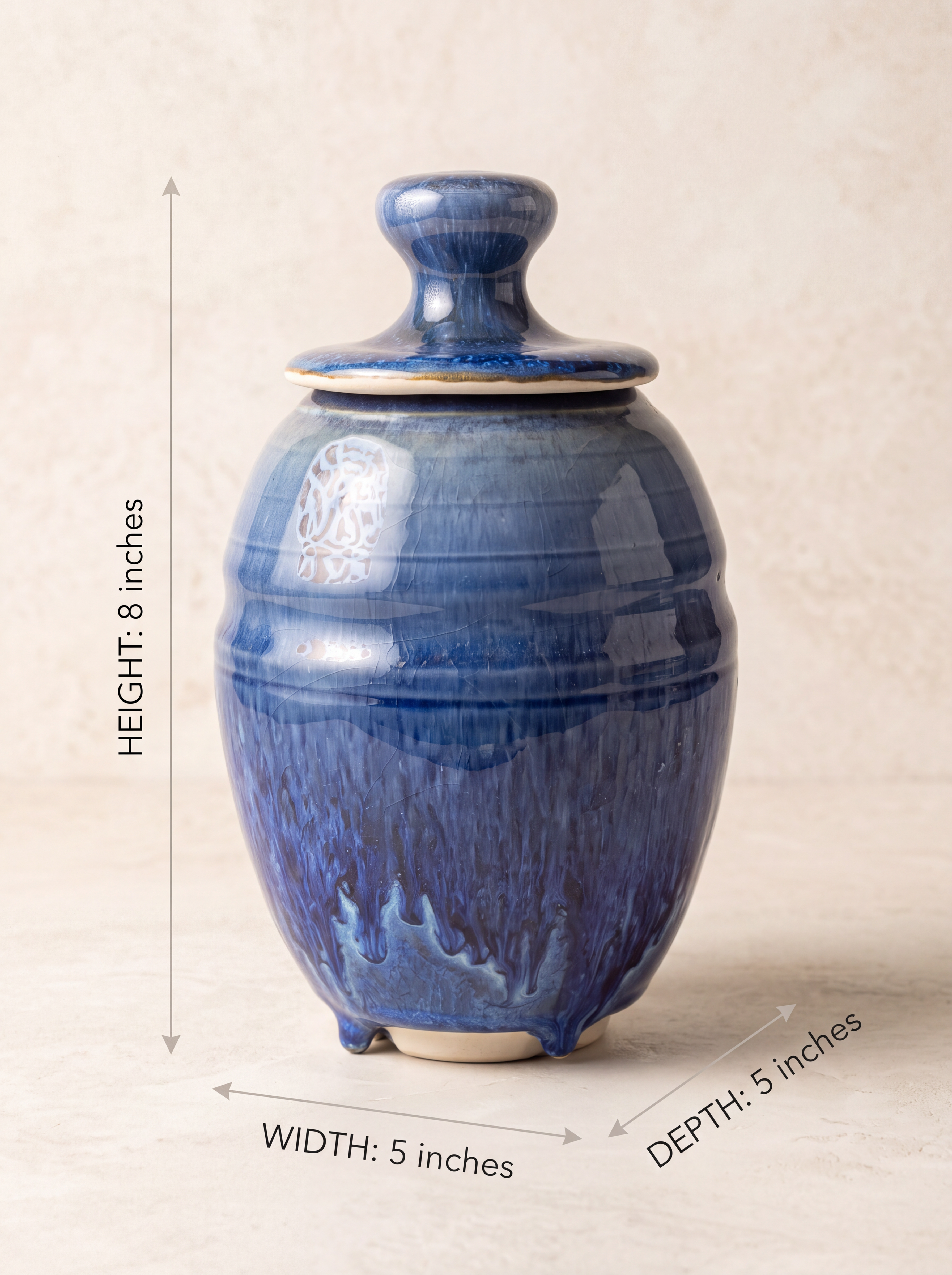 A blue glazed ceramic lidded jar with dimension annotations showing a height of 8 inches, width of 5 inches, and depth of 5 inches on a beige background.